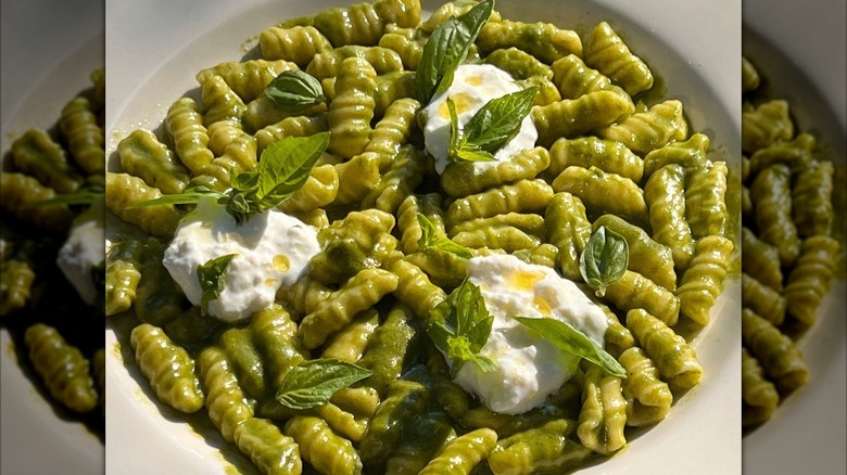 gnocchi in green sauce and fresh cheese in a bowl topped with oil and fresh basil