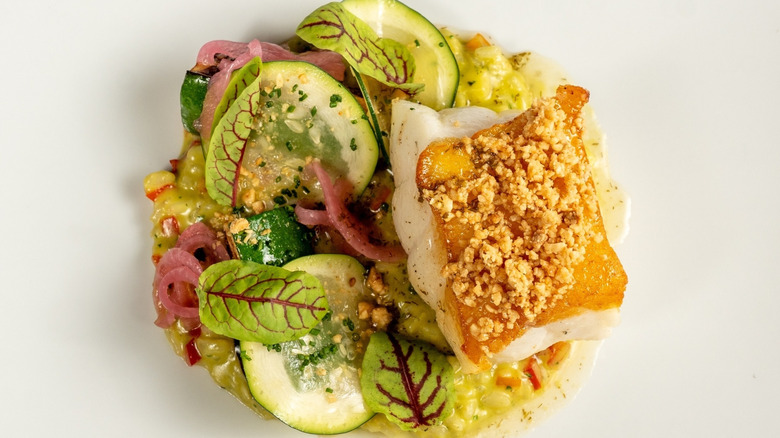 Expertly presented plate of crispy-skinned sea bass topped with crushed hazelnuts, served with cucumbers, pickled red onion, and a green sauce