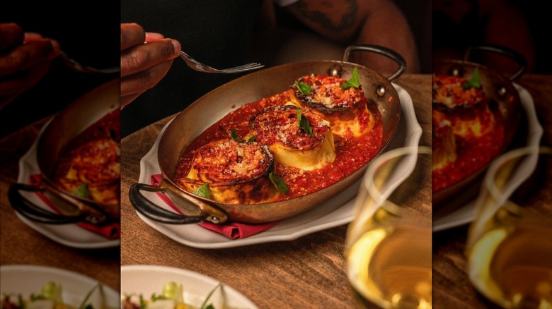 Baked pasta rolls in tomato sauce topped with grated cheese in a silver pan on wooden table