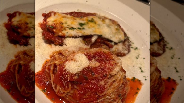 Spaghetti with marinara sauce and grated cheese next to a cut of chicken parmigiana