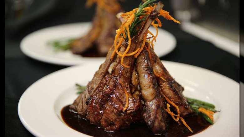 A close-up of glazed lamb chops garnished with a rosemary sprig and fried carrots in soup plate