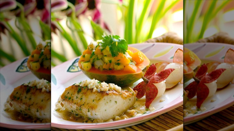 A pan-seared white fish next to fruit salsa in a papaya served with light sauce on plate