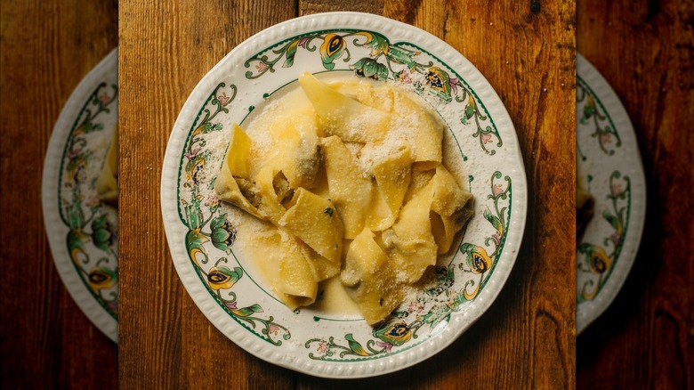 Hand-cut pasta tossed with butter and grated cheese on decorative plate on wooden table