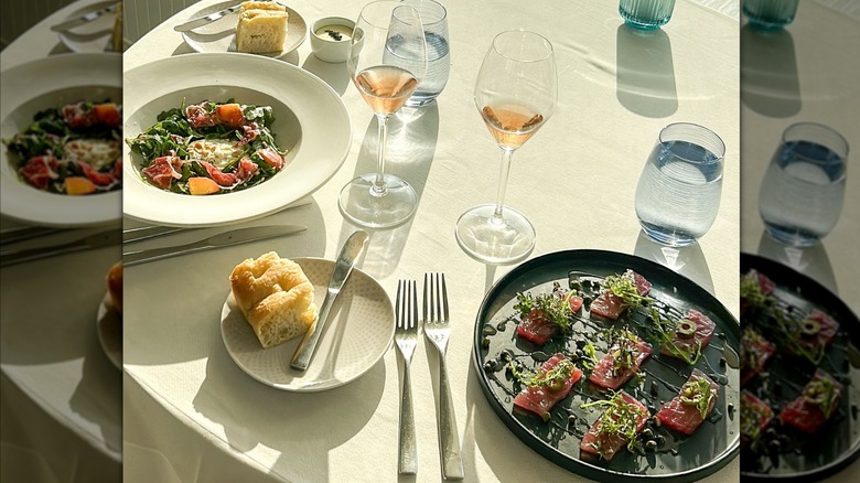 Plates on on table with fine-dining table cloth, glasses of white wine, and bread plates. Setting sun reflecting on table. Colorful dishes consisting of seared cheese, roasted beets, watermelon radish, and mixed greens.