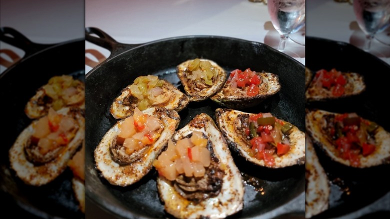 Grilled oysters topped with diced peppers in a cast iron skillet