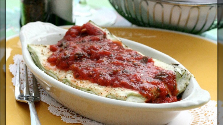 A slice of lasagna in an oval-shaped bowl covered in red suace