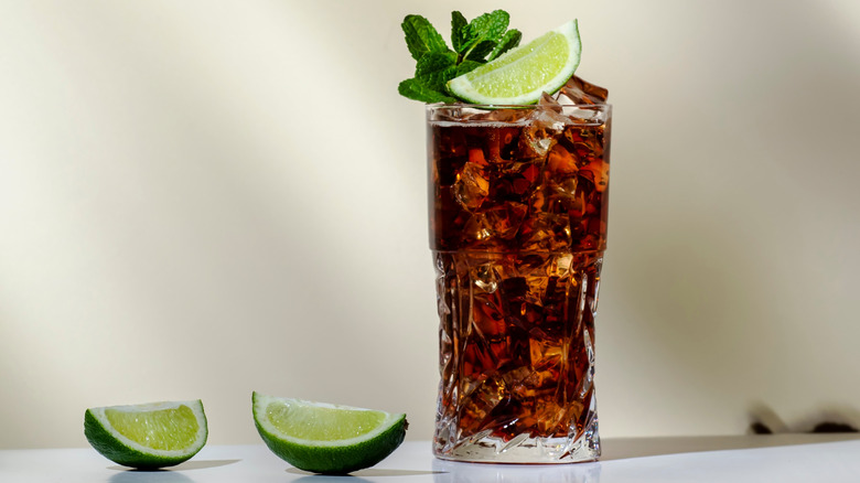 Glass of whisky and Coke with lime wedge and mint