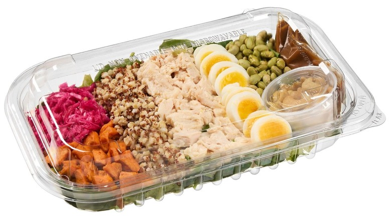 Prepared salad with chicken, grains, hard-boiled eggs, and other ingredients in plastic tray.