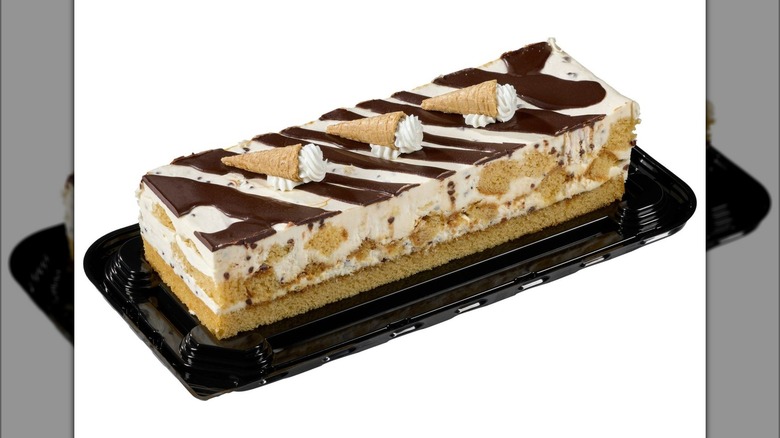 A rectangular cake with chocolate and vanilla ice cream and small waffle cones with whipped cream.