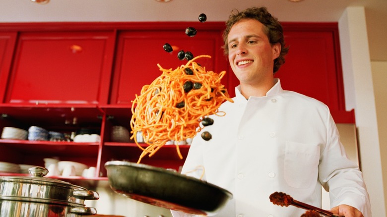 person tossing pasta in pan