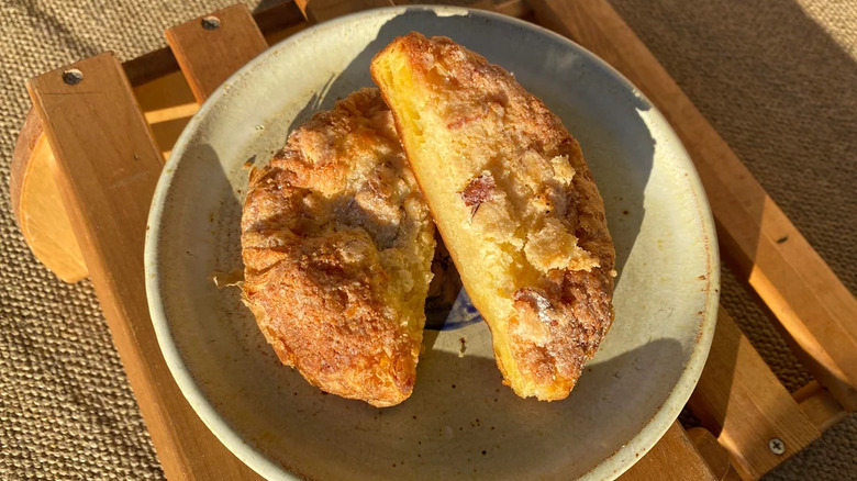 A Costco almond danish cut in half and served on a plate on top of a wooden slatted stool