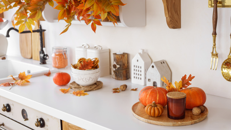 A kitchen with assorted fall themed decor like candles and pumpkins.
