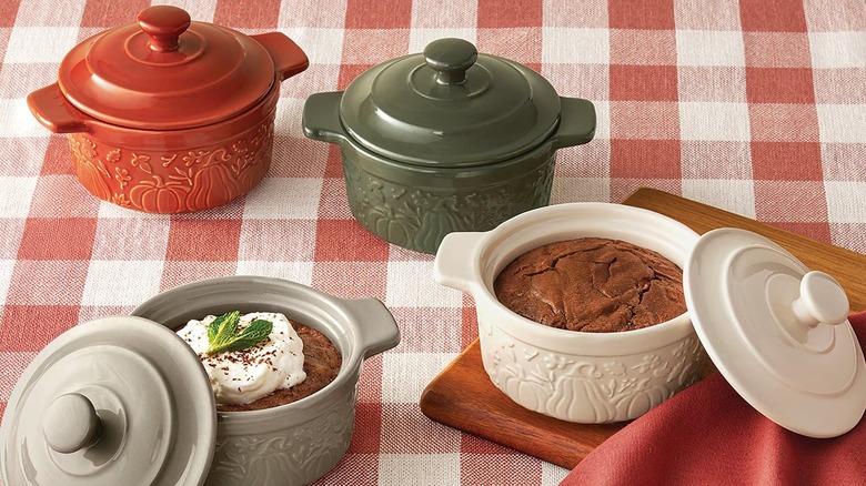Four fall themed stoneware cooking vessels on plaid tablecloth.