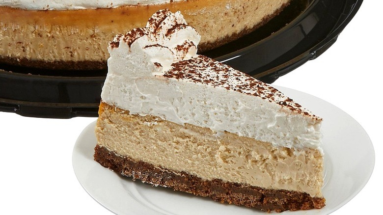 A slice of tiramisu cheesecake from Costco's Kirkland bakery on a small white plate with the cake in the background
