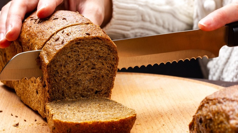 A hand slices a fresh loaf of bread on a wood cutting board