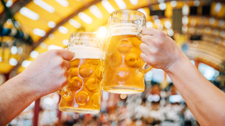 Two people clinking filled German-style beer mugs