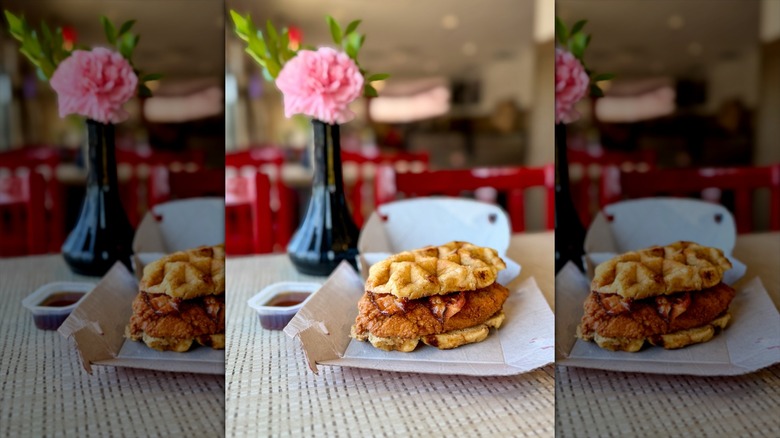 chick fil a chicken and waffles in open cardboard carton on table with flower in vase in background