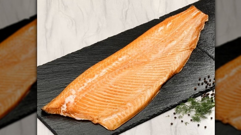 A large whole smoked salmon side on a slate board