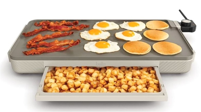 Griddle with bacon, eggs, and pancakes on top with an extending warming drawer filled with potatoes