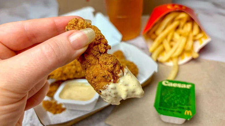 person holding new chicken strip with fries in the background