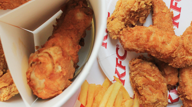 Top view of an open KFC chicken bucket with boneless chicken, chicken tenders, and fries
