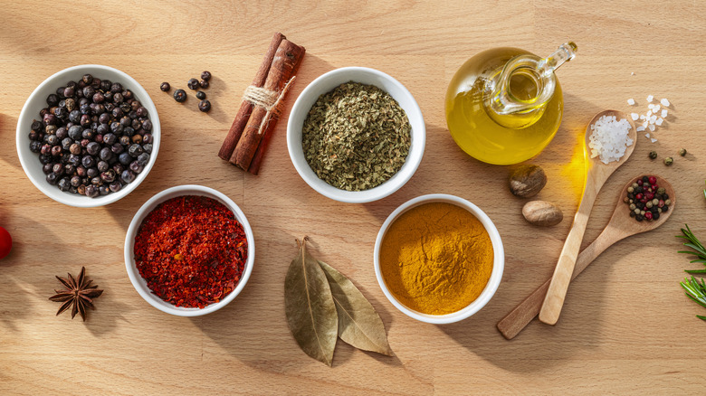 Top-view of white bowls, open bottles, and spoons filled with herbs, oil, and spices