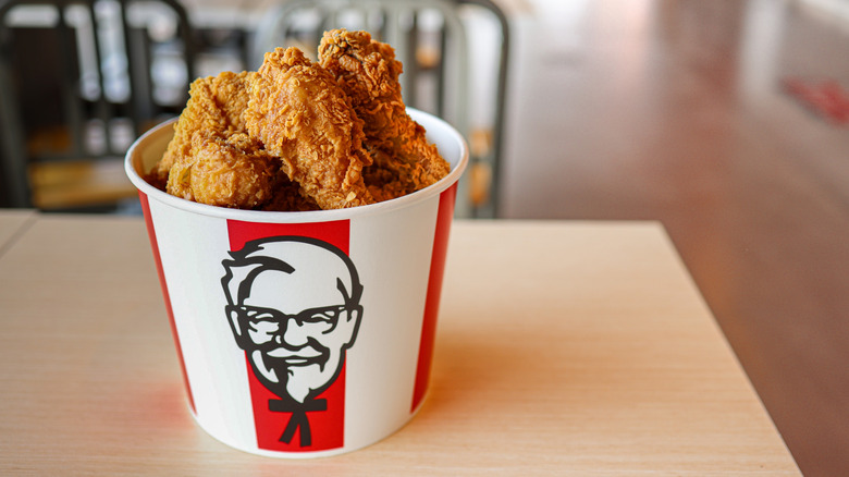 A KFC bucket filled with fried chicken, placed on top of a table in fast food restaurant