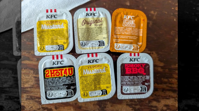 Top-view of six KFC sauce cups on a table, including flavors like mustard, smoky barbecue, and sweet and sour