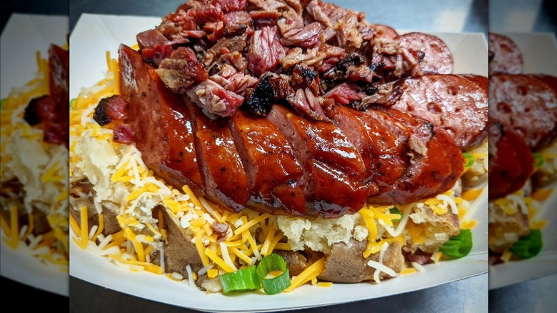 a loaded baked potato topped with barbecue meat and sausage