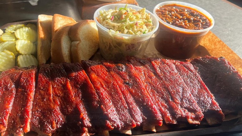 a board of barbecue ribs with beans, coleslaw, Texas toast, and pickles, ready to eat
