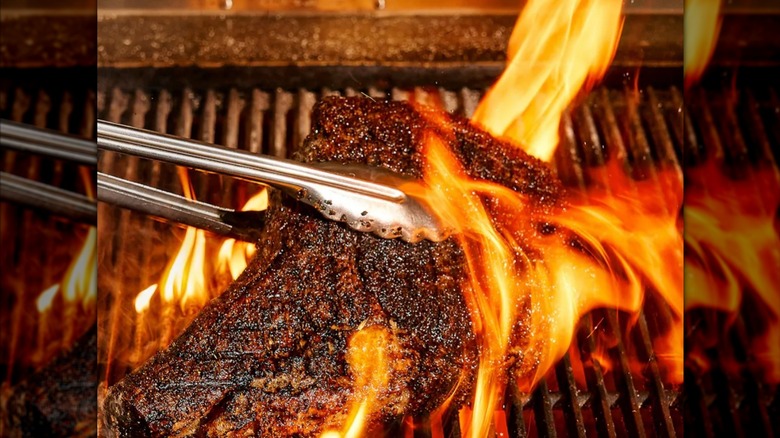tongs flipping over barbecue meat on the grill