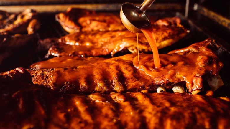 a ladle pouring sauce over ribs cooking on the grill