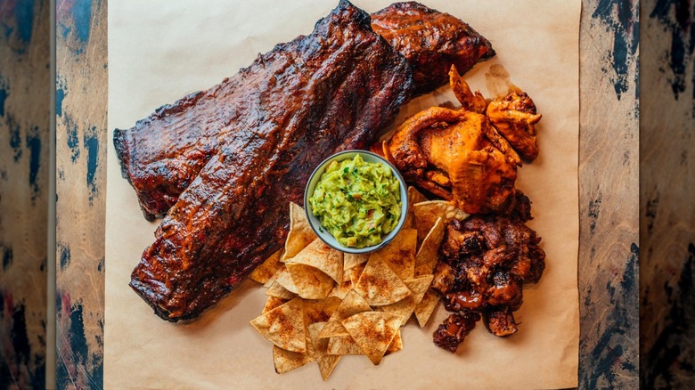 An overhead shot of barbecue ribs with chips, guacamole, and wings