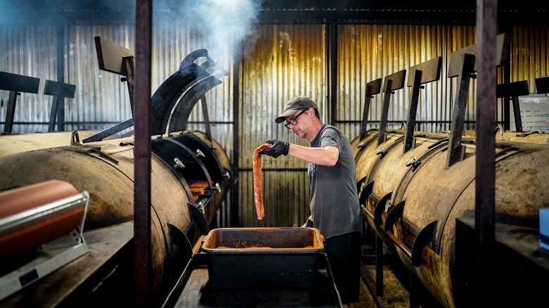 A man holding a raw cut of meat in front of a smoker