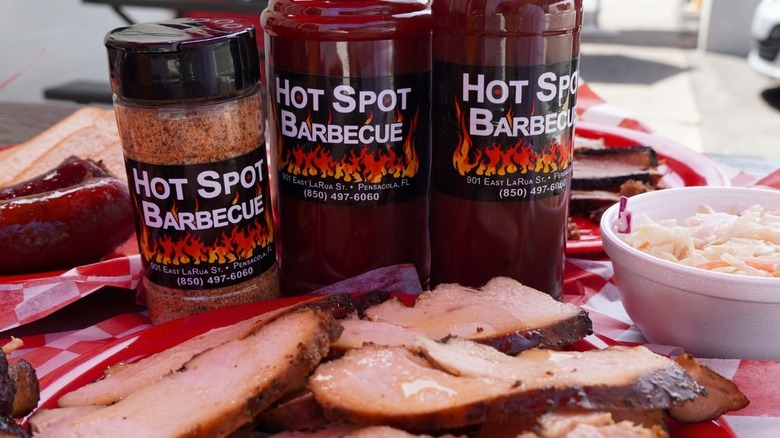 The Hot Spot Barbecue dry rub and barbecue sauce in front of a plate of meat and coleslaw