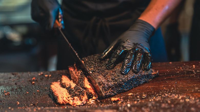 A chef cutting charred meat on a cutting board