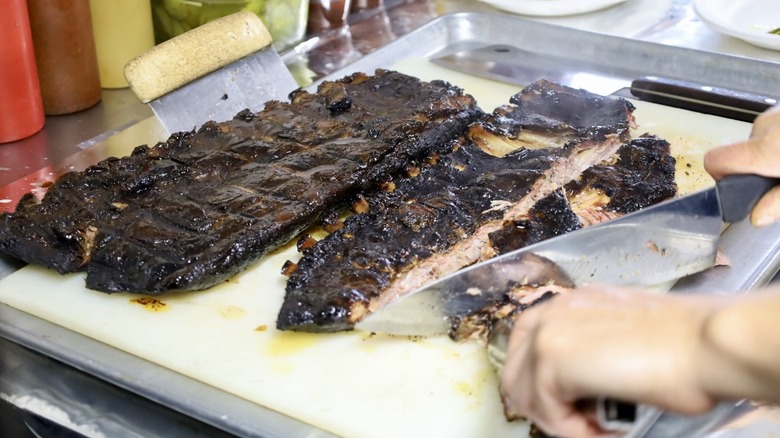 Someone cutting up barbecue ribs on a cutting board