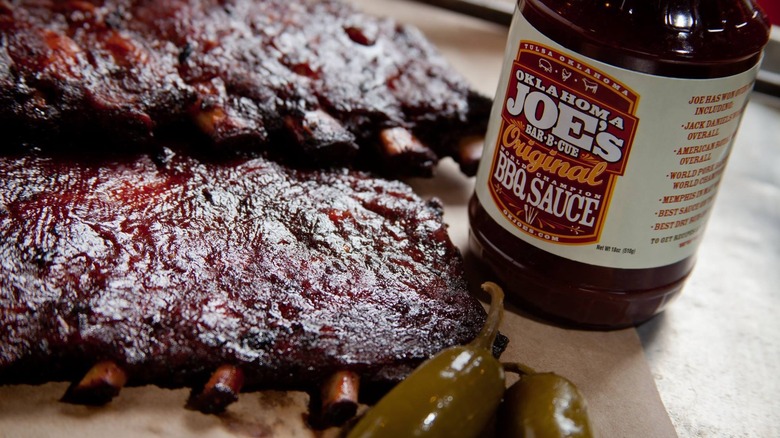 A rack of ribs next to a bottle of Oklahoma Joe's BBQ sauce
