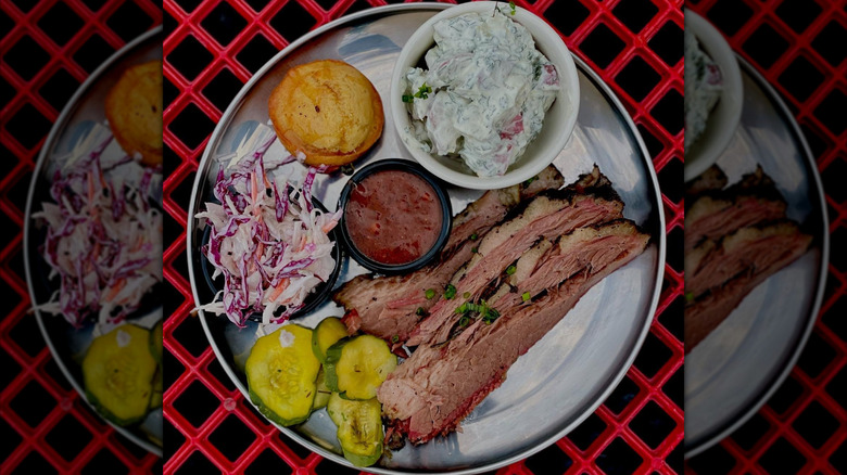 A plate with barbecue, coleslaw, pickles, barbecue sauce, and cornbread