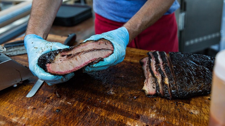 hands holding a piece of barbecue meat above a cutting board