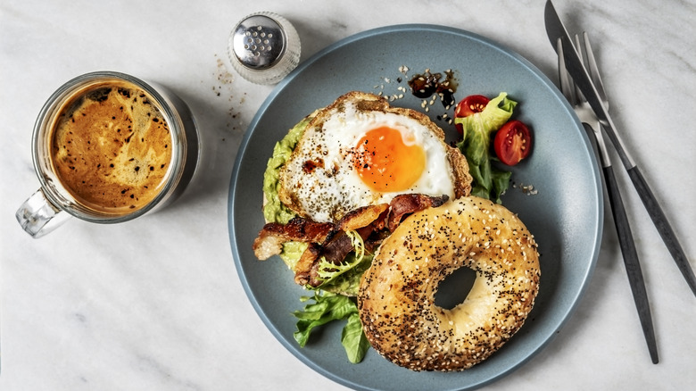 Bagel sandwich on a breakfast table alongside coffee, salt and a fork and knife