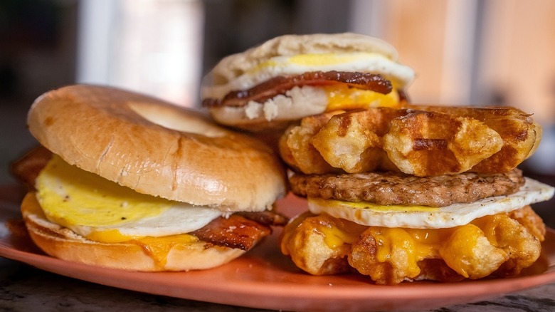 A plate with 3 different sandwiches on different types of bread: regular bread, waffle, and a bagel