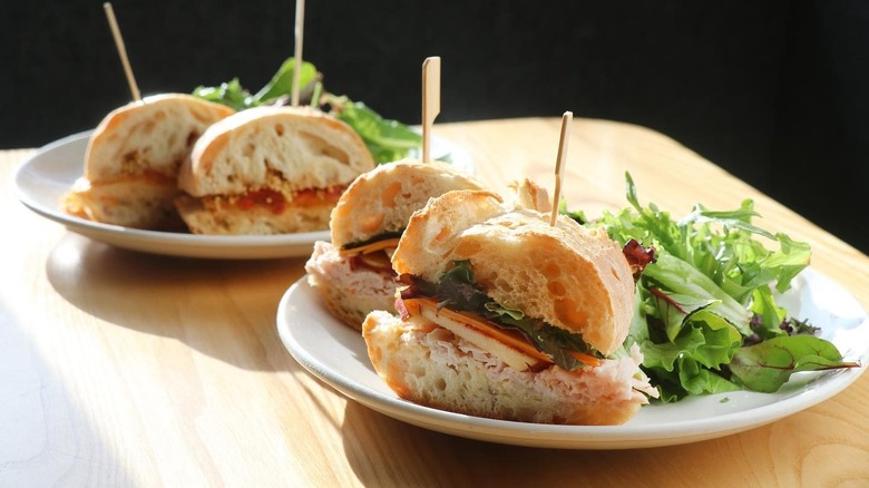 Sandwiches split in half on a table with a side of salad
