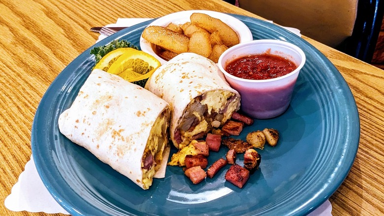 Steak and egg burrito on blue plate with side of potatoes and red sauce