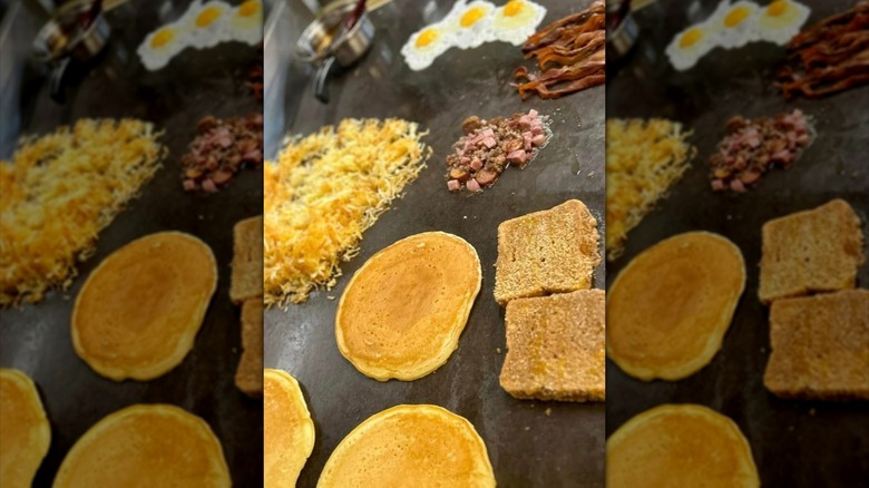 Pancakes, hash browns, bacon, eggs, and toast on griddle