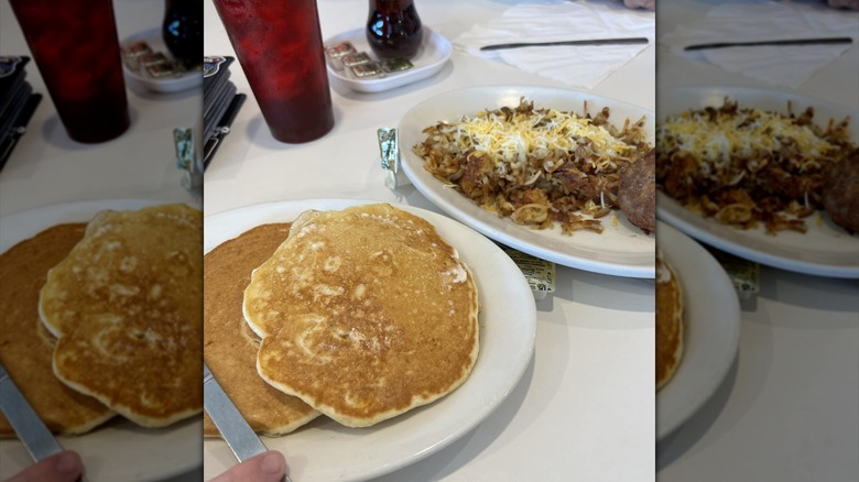 Plate of two pancakes next to plate of hash browns with cheese