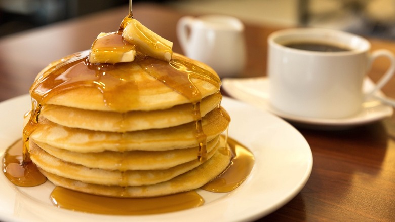 Stack of pancakes topped with butter and maple syrup 