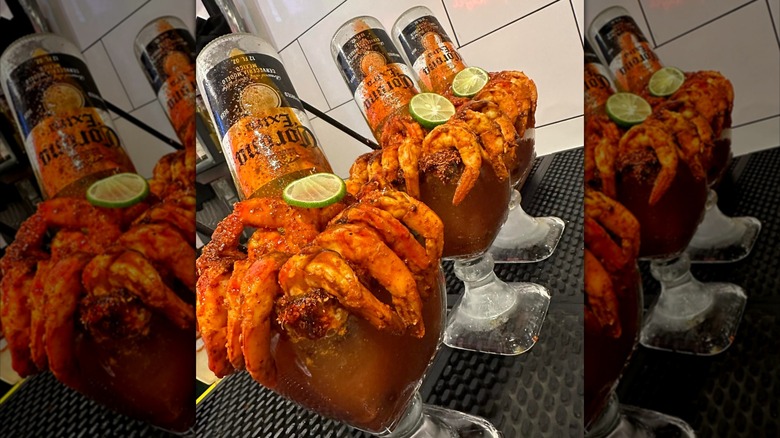 goblets of michelada topped with an overturned corona, seasoned shrimp, and lime