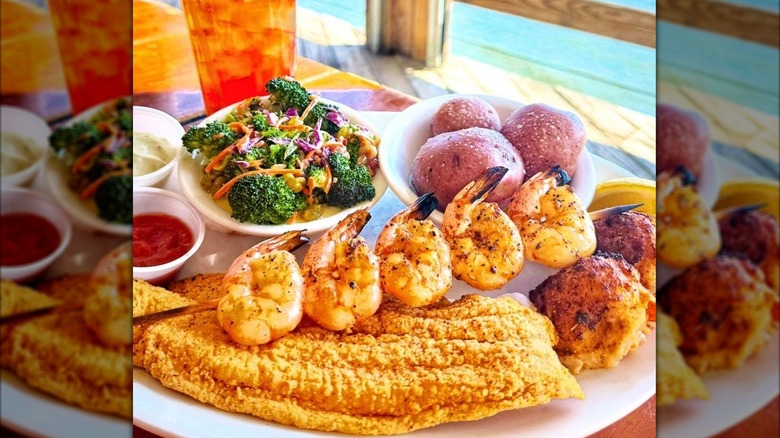 a seafood plate with skewered shrimp, fried fish, crab cakes, veggies, and baby potatoes