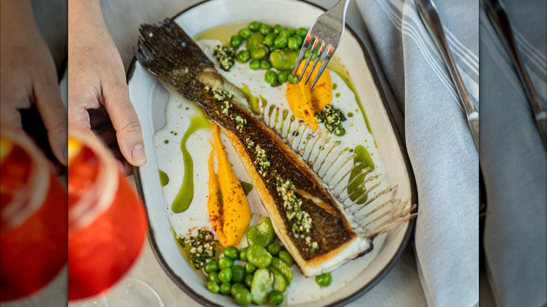 prepared piece of fish served on a plate with peas and sauce